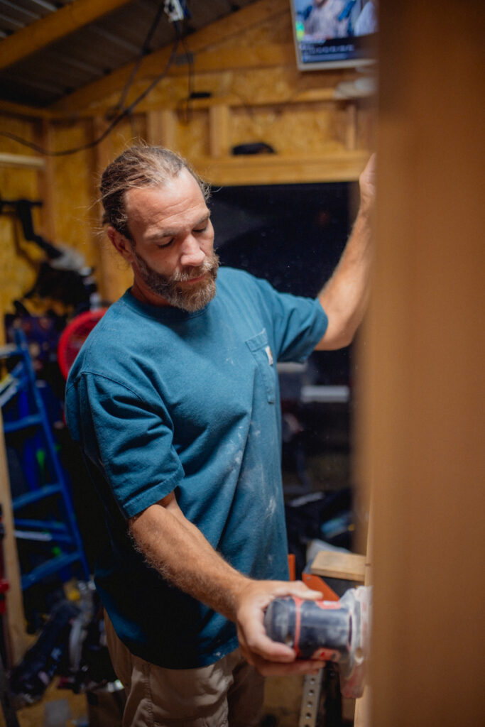 Dustin Dalton sanding a custom pantry cabinet in his woodworking shop.